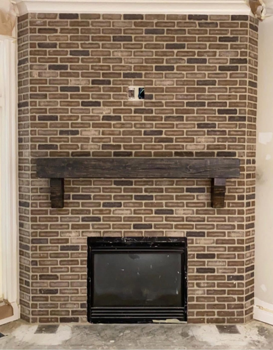 Floor-to-ceiling brown brick fireplace with a rustic wood beam mantel