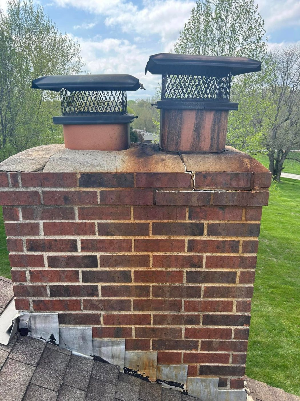Brick chimney stack with a cracked crown and stained flue caps